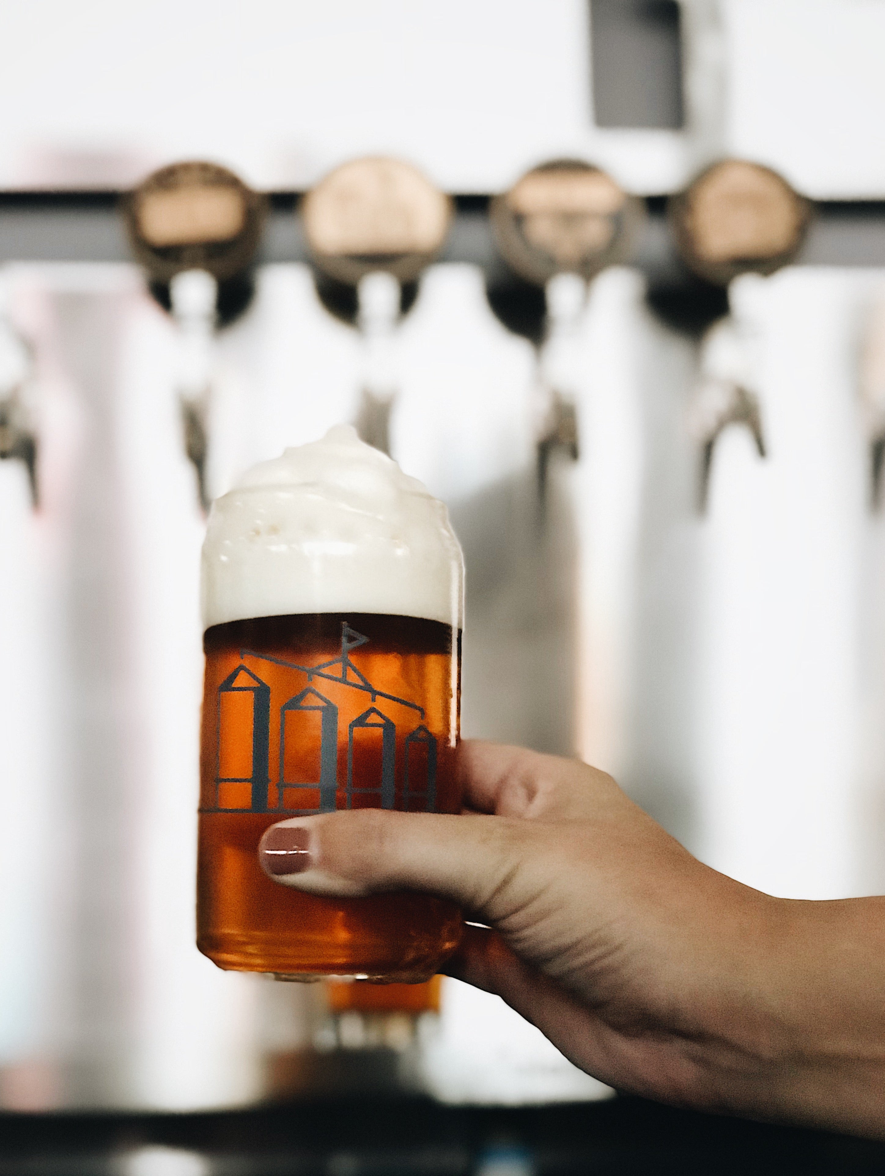Hand holding a glass of beer with a blurred background of beer taps