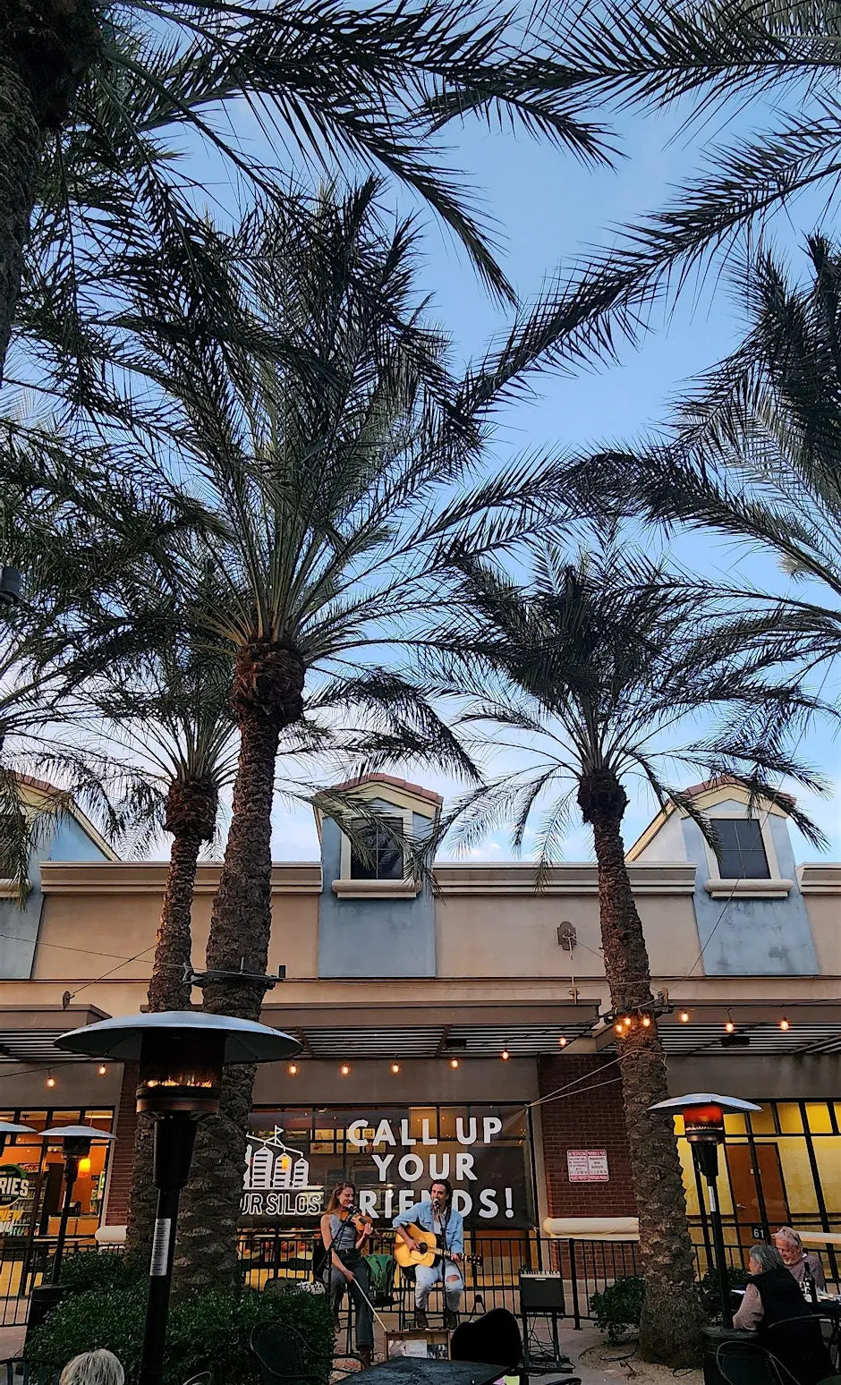 Outdoor setting with palm trees and a building facade, featuring a sign that says 'Call Up Your Friends'.